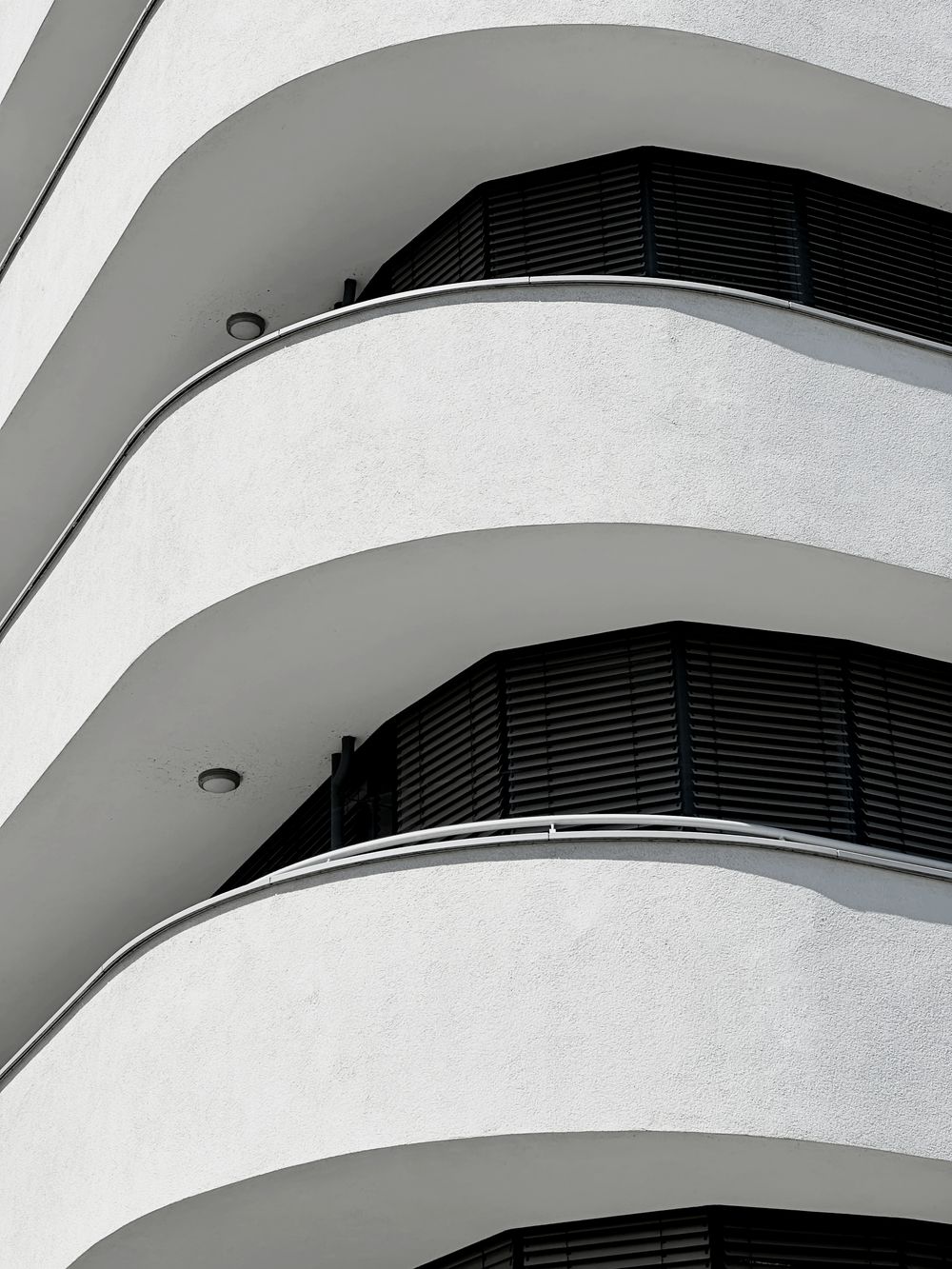 Balcons arrondis en béton blanc d’un immeuble de logements récent, superposés étage après étage.
