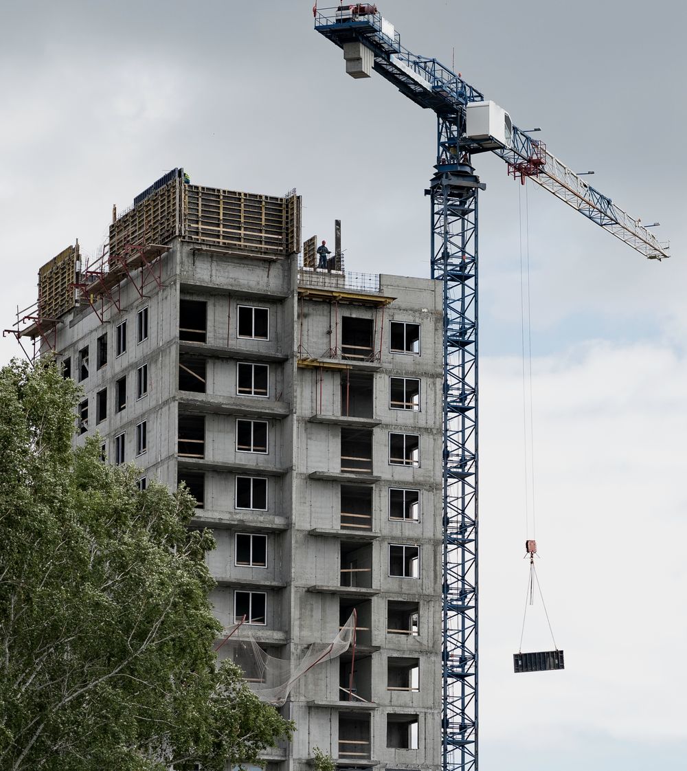 Immeuble de logements en construction, dalles de béton et coffrages au sommet, grue à tour déployée à côté.