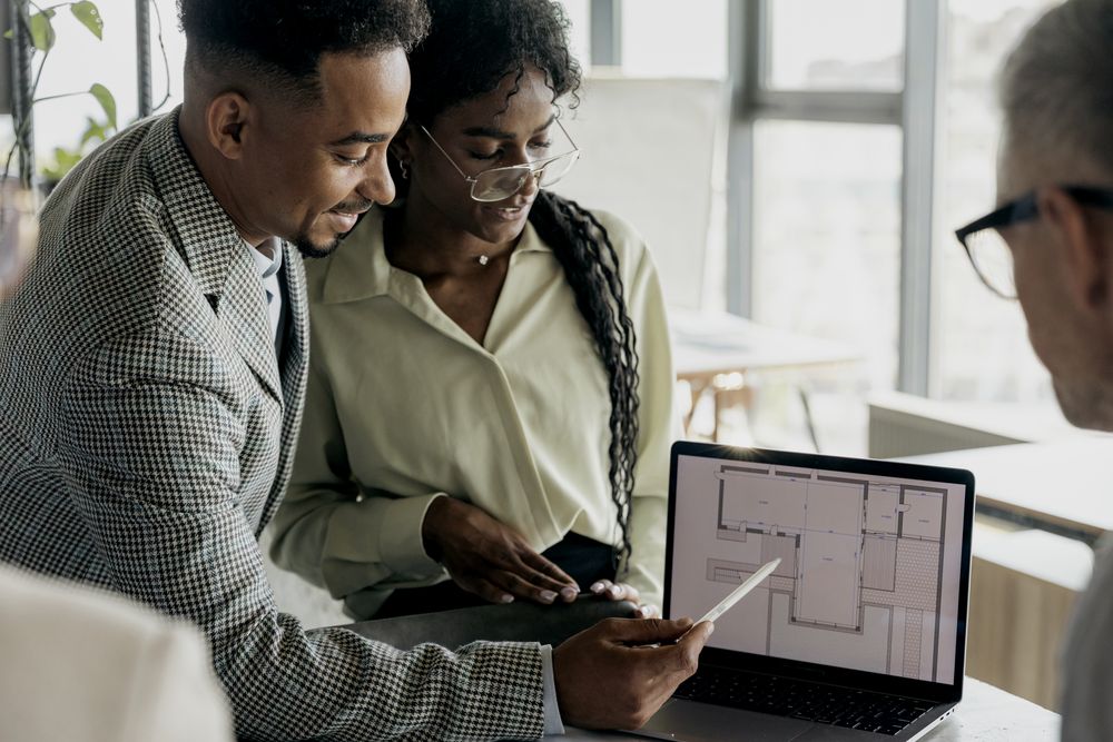 Un couple regarde avec un conseiller le plan d’un appartement affiché sur un ordinateur portable.